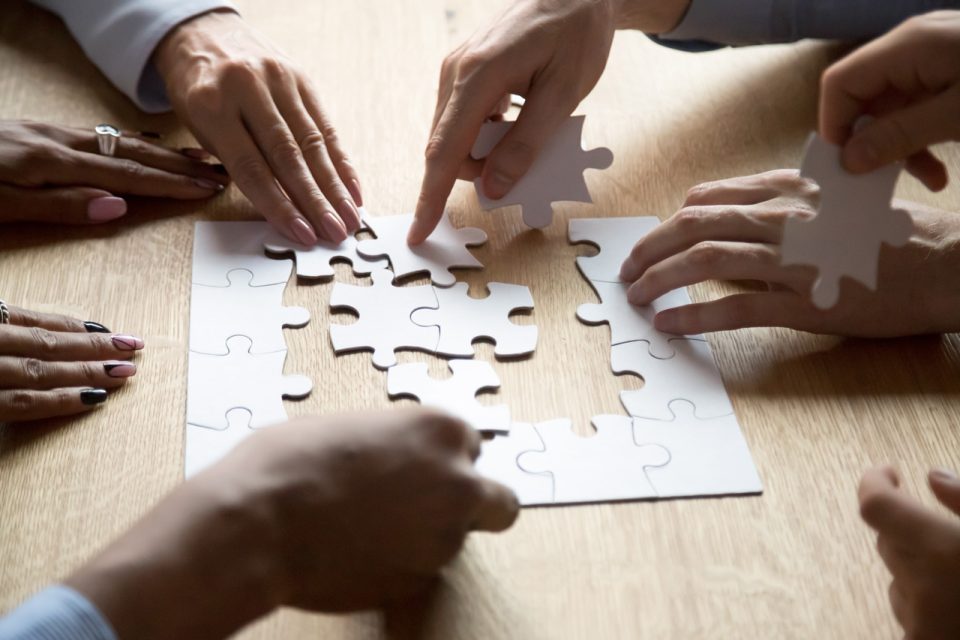 Multiple pairs of hands work on a puzzle together on a wood table