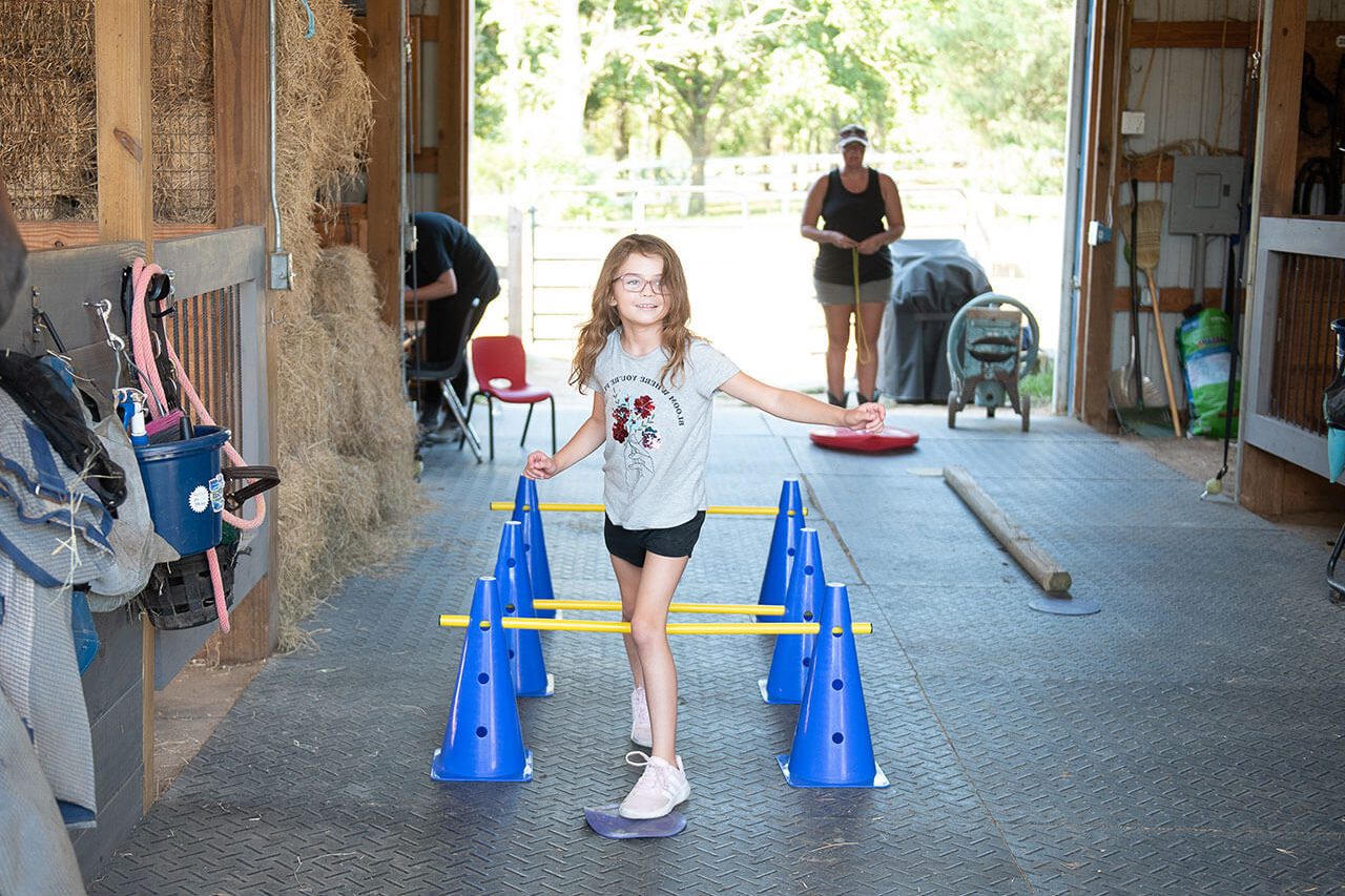 A young girl performs an exercise in a horse barn during a hippotherapy session
