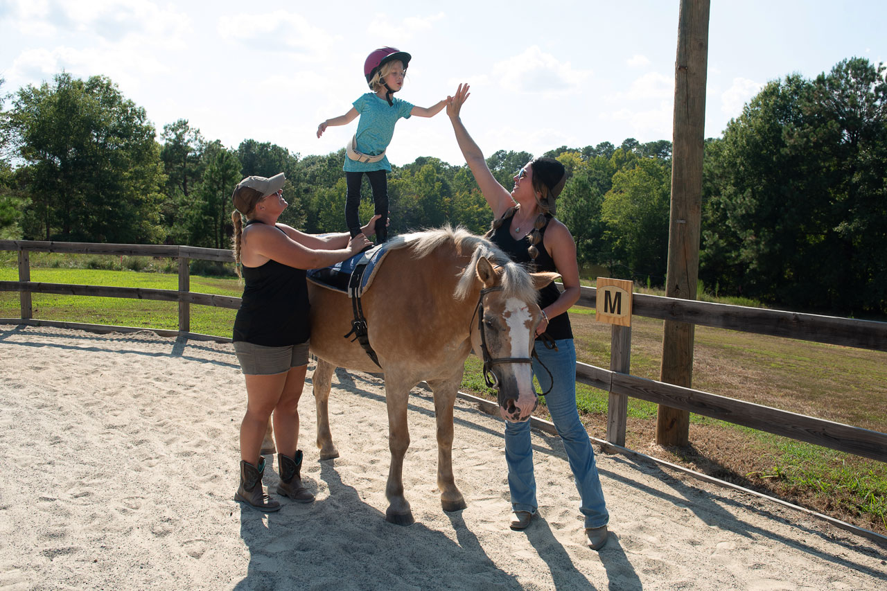 Young blond girl stands on a horse during a hippotherapy session at Carolina Therapeutic Ranch in Rock Hill, SC