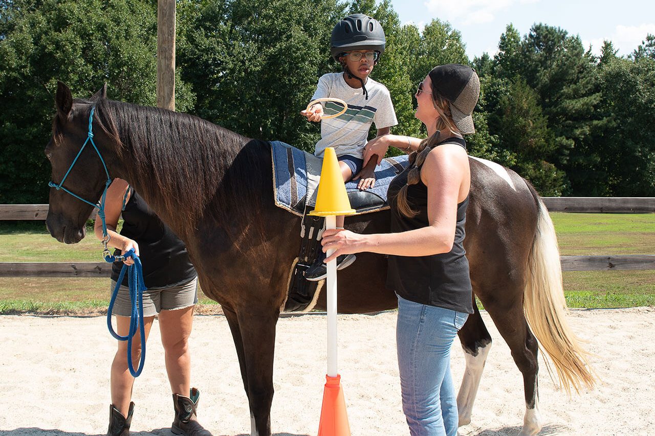 A young boy throws a ring on a cone while on horseback during a hippotherapy session at Carolina Therapeutic Ranch in Rock Hill, SC