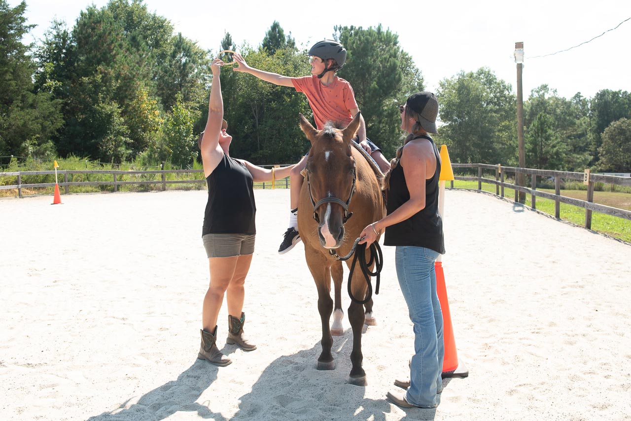 A child reaches for a ring while on horseback during a hippotherapy session