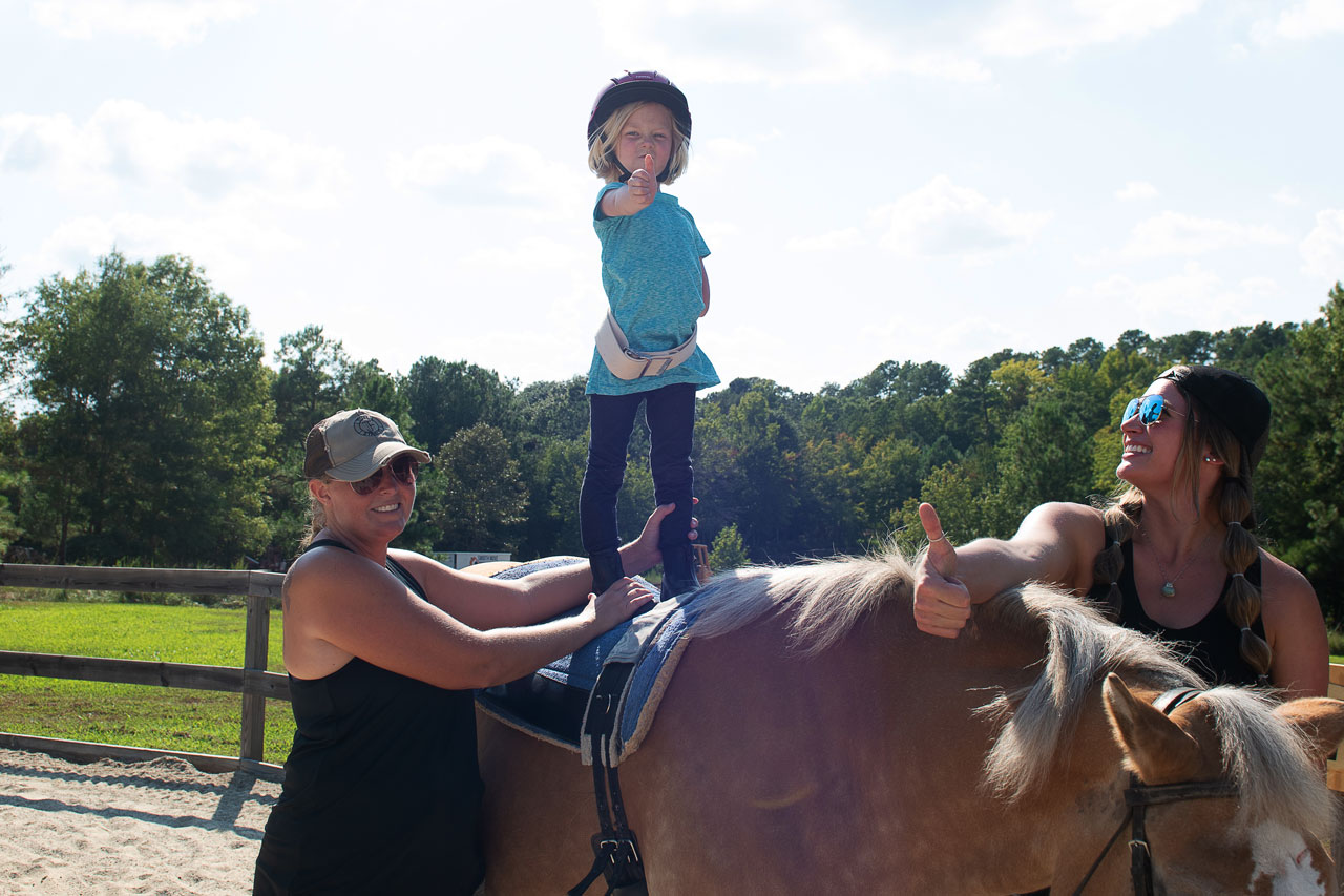 Young blond girl stands on a horse during a hippotherapy session at Carolina Therapeutic Ranch in Rock Hill, SC